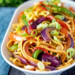 Stir fried sweet chilli noodles with peppers, red onions garnished with spring onion.