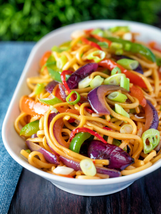 Stir fried sweet chilli noodles with peppers, red onions garnished with spring onion.