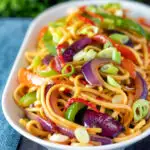 Stir fried sweet chilli noodles with peppers, red onions garnished with spring onion featuring a title overlay.