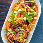 Overhead stir fried sweet chilli noodles with peppers, red onions garnished with spring onions.