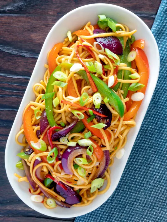 Overhead stir fried sweet chilli noodles with peppers, red onions garnished with spring onions.