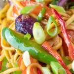 Clos up stir fried sweet chilli noodles with peppers, red onions garnished with spring onions featuring a title overlay.