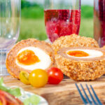 Picnic spread with oven baked scotch eggs cut open to show a jammy yolk featuring a title overlay.