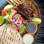 Overhead beef kofta kebabs served with salad, pita bread and sauces.