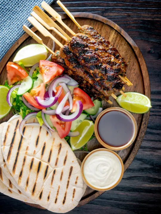 Overhead beef kofta kebabs served with salad, pita bread and sauces.