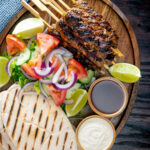 Overhead beef kofta kebabs served with salad, pita bread and sauces featuring a title overlay.