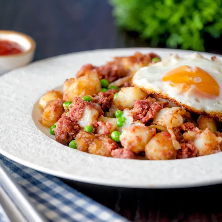 Canned corned beef hash with fried egg and garden peas.