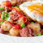 Canned corned beef hash with fried egg and peas and tomato ketchup.