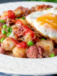 Canned corned beef hash with fried egg and peas and tomato ketchup.