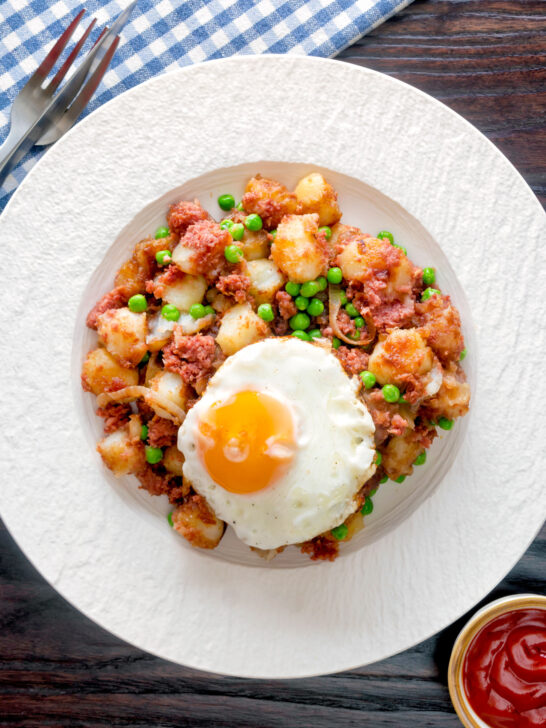 Overhead canned corned beef hash with fried egg and peas.