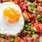 Close up overhead canned corned beef hash with fried egg and peas and ketchup.