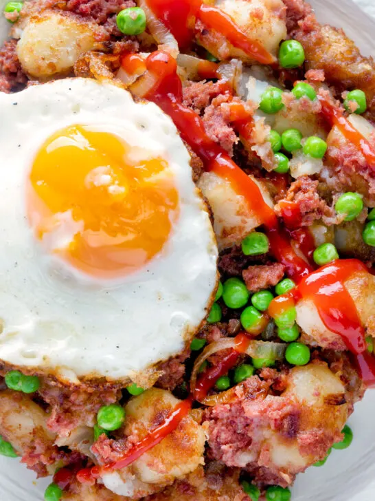 Close up overhead canned corned beef hash with fried egg and peas and ketchup.