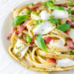 Cod pasta with pesto, peas and bacon served on a white plate.