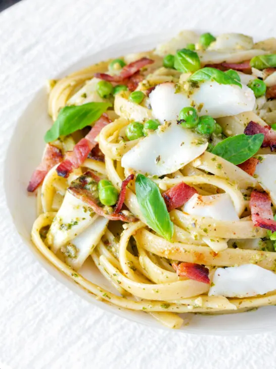 Cod pasta with pesto, peas and bacon served on a white plate.