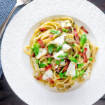 Overhead cod pasta with pesto, peas and bacon served on a white plate.