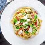 Overhead cod pasta with pesto, peas and bacon served on a white plate.