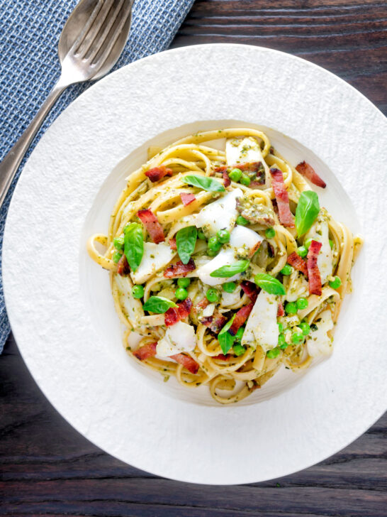 Overhead cod pasta with pesto, peas and bacon served on a white plate.