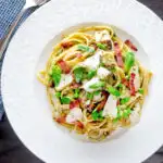 Overhead cod pasta with pesto, peas and bacon served on a white plate featuring a title overlay.