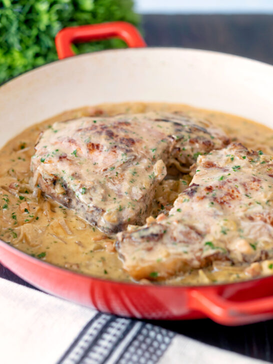 Normandy pork chops in a creamy cider and apple sauce in an enamel cooking pan.