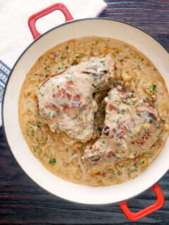 Overhead Normandy pork chops in a creamy cider and apple sauce in an enamel pan.
