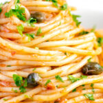 Close up tomato tuna pasta with capers and fresh parsley.