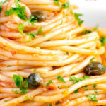 Close up tomato tuna pasta with capers and fresh parsley featuring a title overlay.