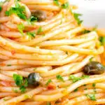 Close up tomato tuna pasta with capers and fresh parsley featuring a title overlay.