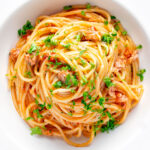 Overhead tomato tuna pasta with capers and fresh parsley.