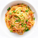 Overhead tomato tuna pasta with capers and fresh parsley.