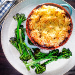 Overhead sausage and mash pie served with roasted tenderstem broccoli.
