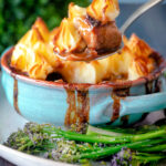 Spoon taking a serving of Sausage and mash pie with roasted tenderstem broccoli.