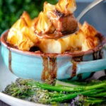 Spoon taking a serving of Sausage and mash pie with roasted tenderstem broccoli.