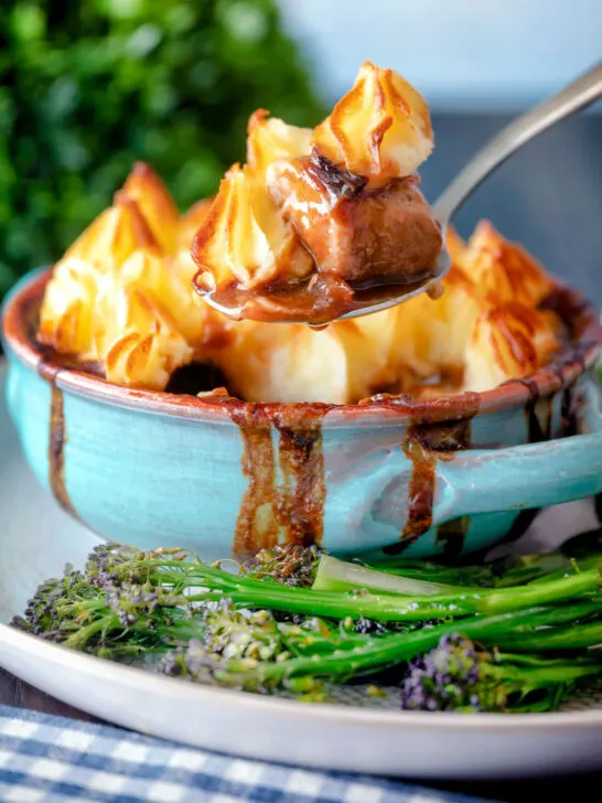 Spoon taking a serving of Sausage and mash pie with roasted tenderstem broccoli.