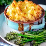 Sausage and mash pie served with roasted tenderstem broccoli featuring a title overlay.