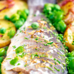 Close up baked or roasted sea bass with new potatoes, peas, broad beans and bacon.
