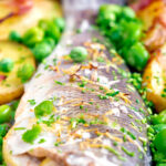 Close up baked or roasted sea bass with new potatoes, peas, broad beans and bacon featuring a title overlay.