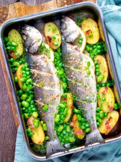 Overhead baked or roasted sea bass with new potatoes, peas, broad beans and bacon.