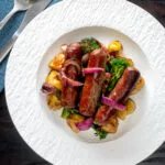 Overhead sausage and potato tray bake with onions and broccoli served on a plate.