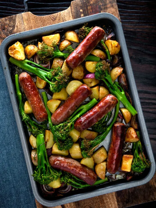 Overhead sausage and potato tray bake with onions and tenderstem broccoli.