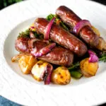 Sausage and potato tray bake with onions and broccoli served on a plate.