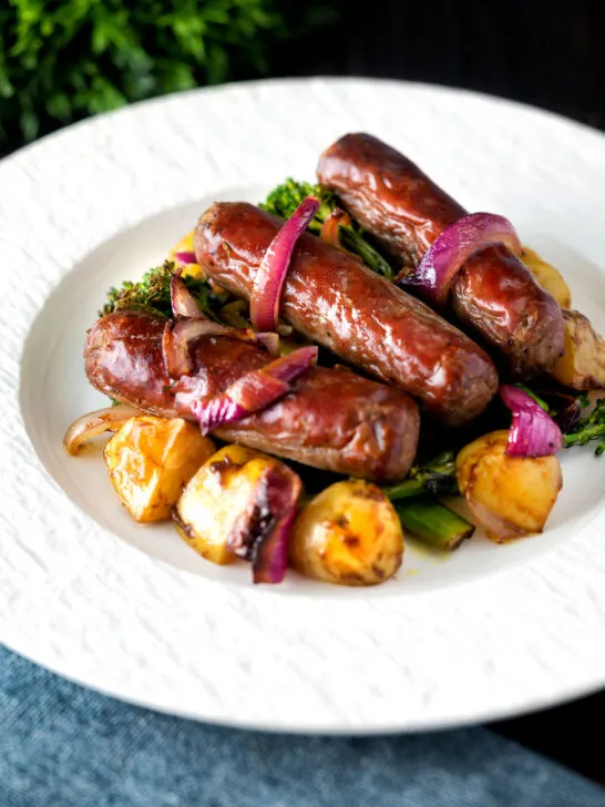 Sausage and potato tray bake with onions and broccoli served on a plate.