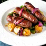 Sausage and potato tray bake with onions and broccoli served on a plate featuring a title overlay.