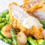 Close up oven baked cornflake coated chicken breast served with mustard sauce and veggies.