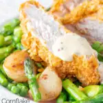 Close up oven baked cornflake coated chicken breast served with mustard sauce and veggies featuring a title overlay.