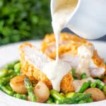 Mustard sauce being poured over a cornflake crusted chicken breast.