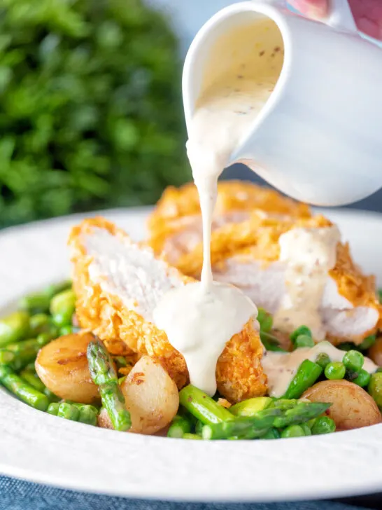 Mustard sauce being poured over a cornflake crusted chicken breast.