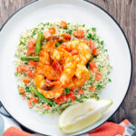 Overhead Moroccan influenced garlic harissa prawns served with couscous.