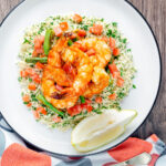 Overhead Moroccan influenced garlic harissa prawns served with couscous featuring a title overlay.