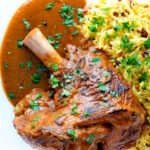 Overhead close up lamb shank curry or nalli gosht served with pilau rice featuring a title overlay.