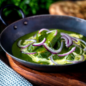 Palak chicken or murgh curry with red onions and cream served in an iron karai.